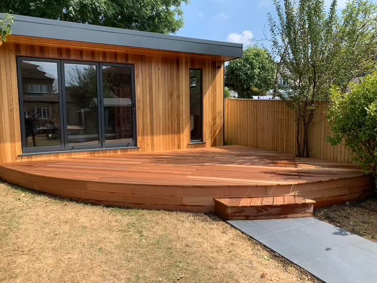 Cedar-clad garden room with a curved hardwood deck, a single wide step and a grey porcelain path leading to it